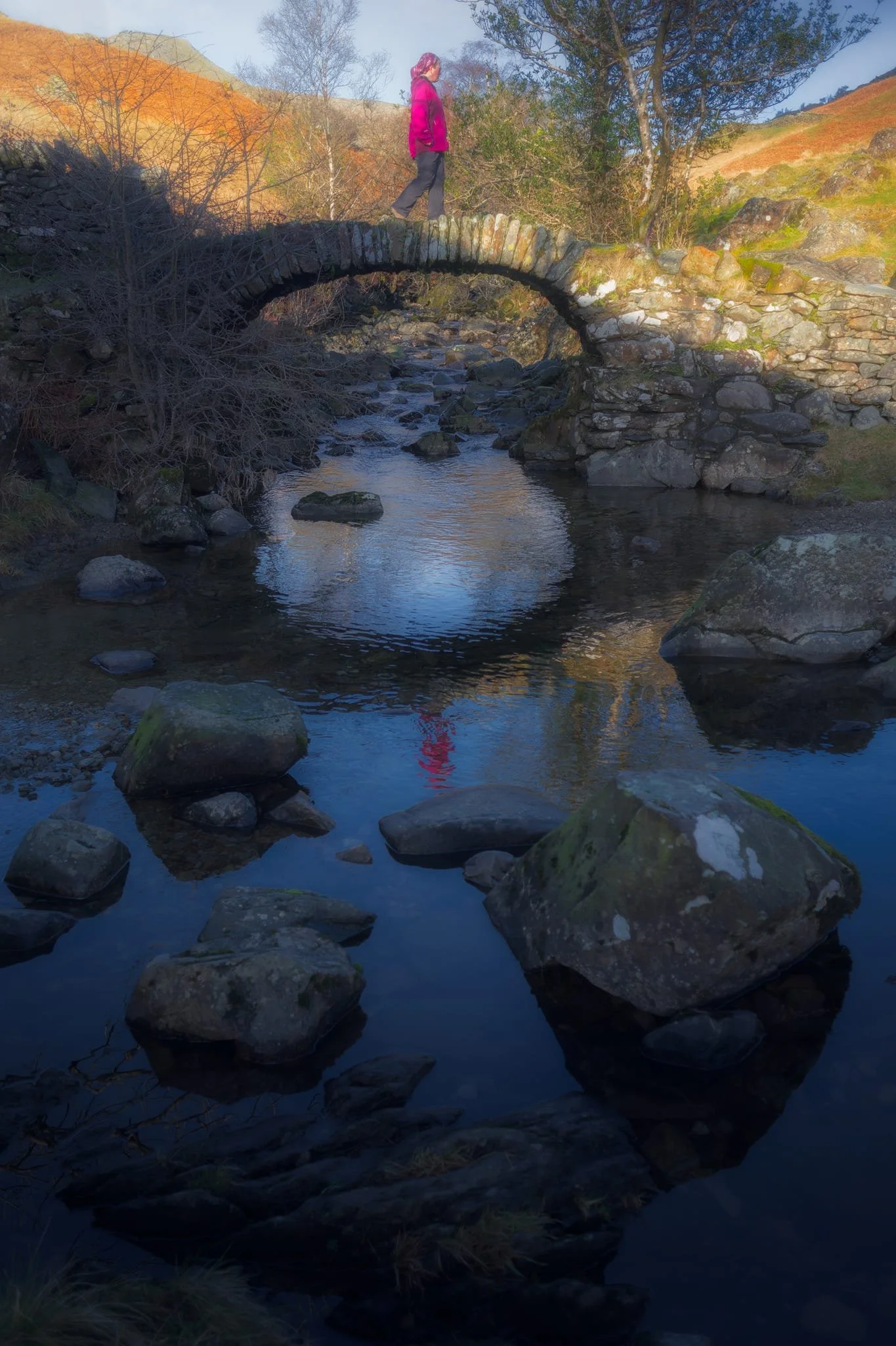 The old packhorse bridge itself, with my Lisabet providing a nice colour contrast as she strolls across it. As I’ve mentioned on this site elsewhere, the name “High Sweden Bridge” might seem unusual, given this is located in the Lake District, England. The “sweden” aspect originally comes from the Old Norse sviðin (pronounced “swee-thin”), the past participle of svíða , meaning “to burn” or “to singe”. In this context, it refers to the clearing of land by burning.
