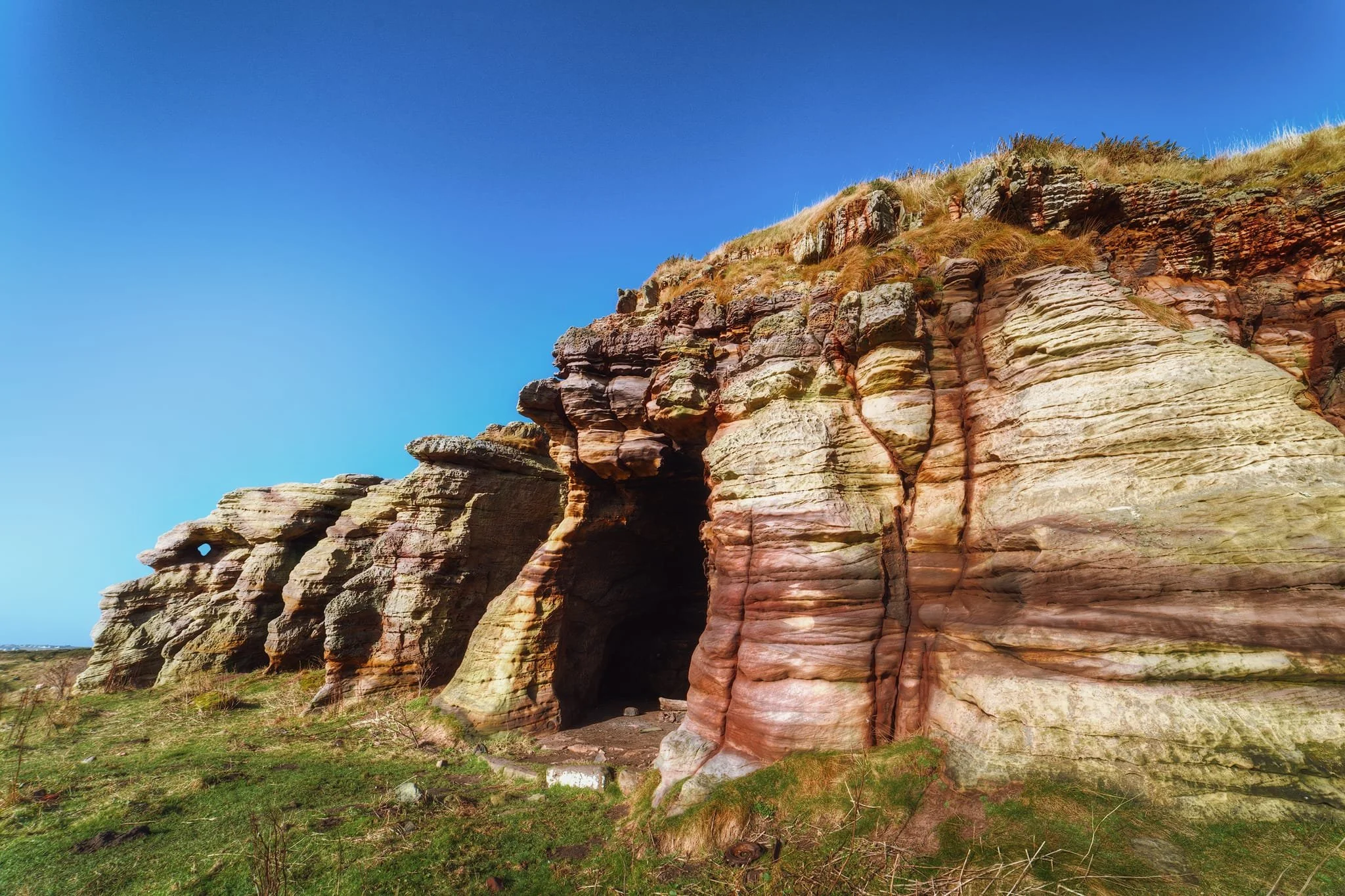  Roughly halfway between Anstruther and Crail this striking formation suddenly arrests your attention. These are the Caiplie Caves. They feature beautiful formations from around 370 to 360 million years ago. They&rsquo;re notable for their bright stripes of pink, red, yellow, and cream colours, which show how the environment changed when the rocks were formed in ancient river systems and floodplains. The caves were shaped over time by the action of sea waves, which gradually wore away the softer rock layers while leaving the harder ones intact. This process created natural shelters along cracks in the rock, which were important as refuges for early Christian settlers in the coastal area of Fife. Isn&rsquo;t it fascinating? 