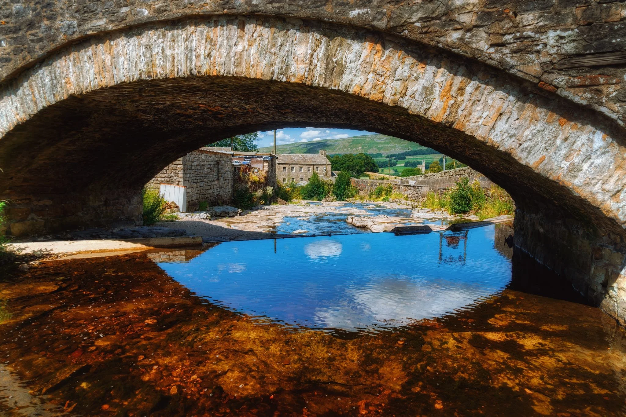 Near Gayle Mill, Lisabet and I clamber down alongside the old stone for some shots around Gayle Beck. I get low underneath for this shot towards Gayle Mill and Wensleydale fells beyond.