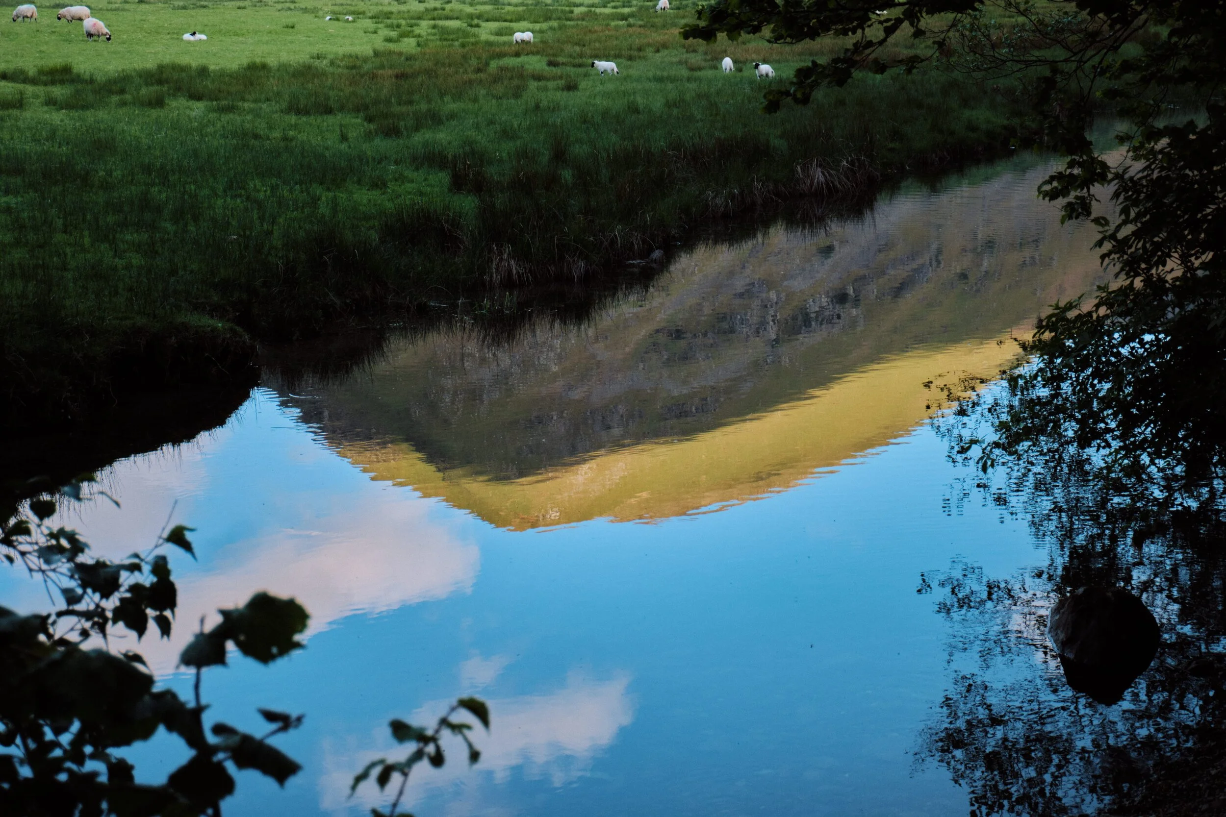 The lit summit of Hartsop Dodd (618 m/2,028 ft) reflected in the still water of Goldrill Beck near Brotherswater.