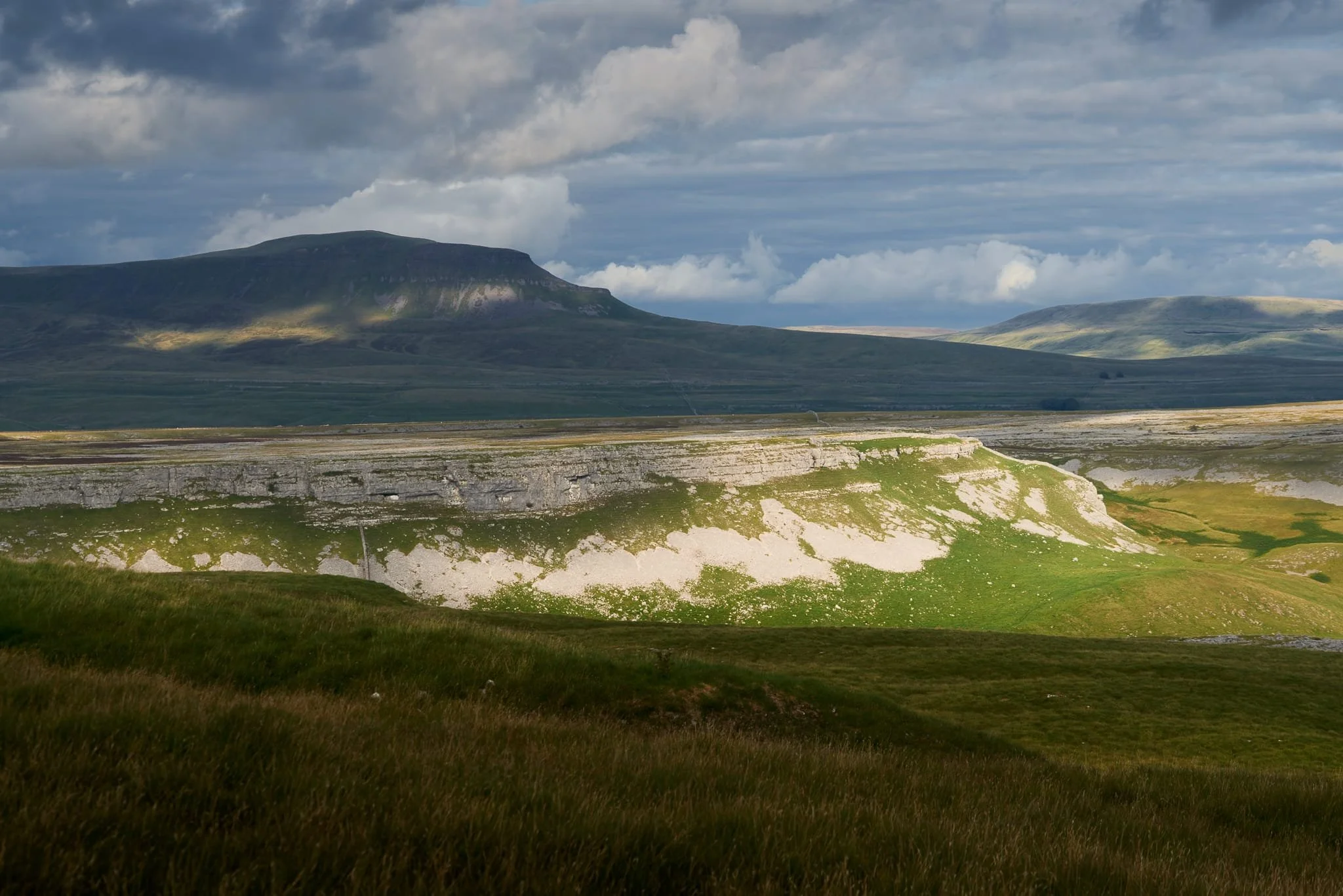 One last look back at Pen-y-Ghent as the last of the dark clouds cast the fell in deep shadow. Beneath, the edge of Moughton Scar is illuminated.