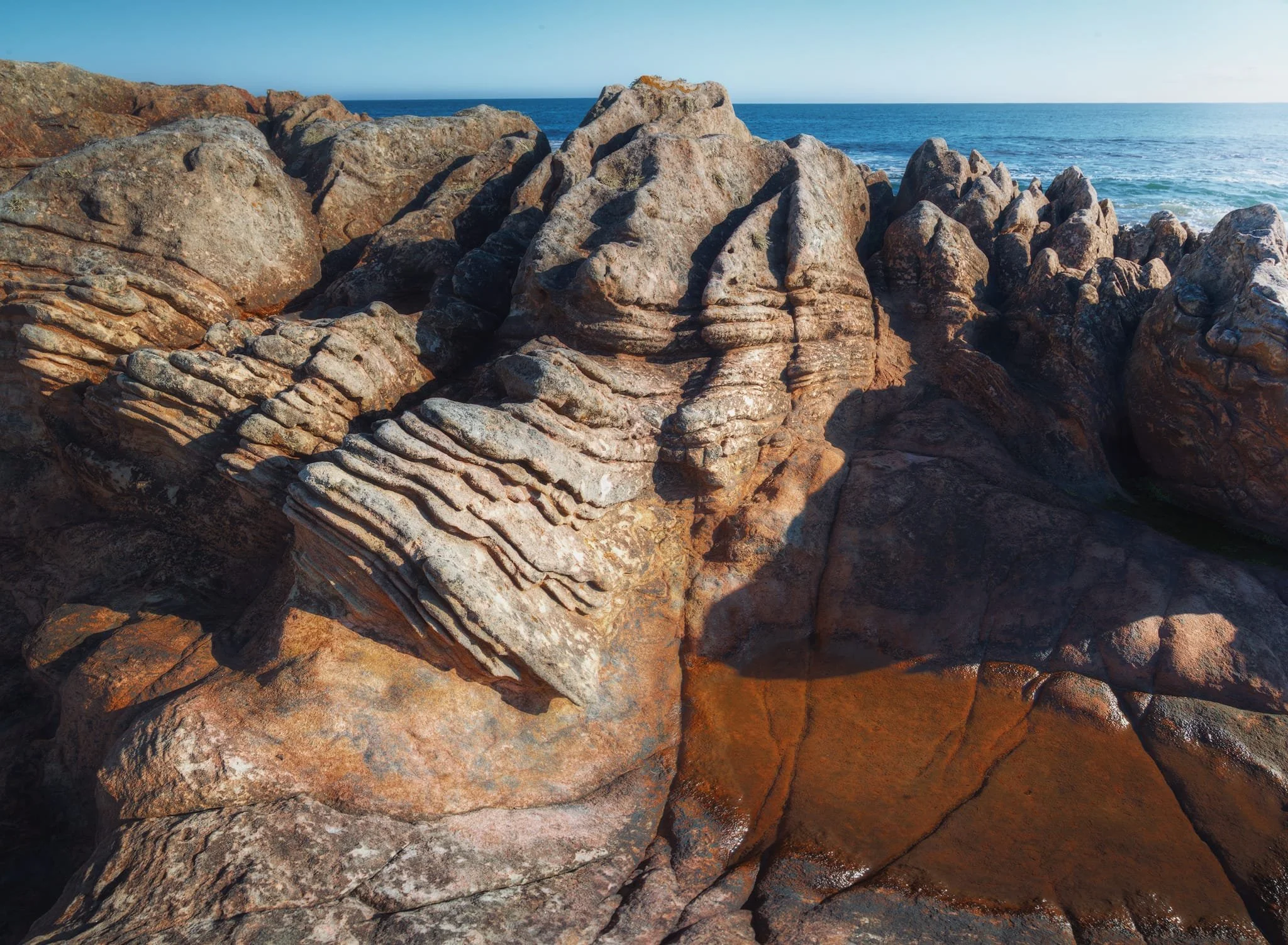  A panorama of five vertical shots, stacked left to right, shows the impressive layers of sedimentary rock made of pinkish-brown sandstone. The layers form ridges that tell the story of how this rock was formed. Some of the rock is tilted as well, having been affected by movements in the Earth&rsquo;s crust. You can also see different patterns of cracks in the rock, creating angular pieces that have weathered over time into various colors. Nature is an artist. 