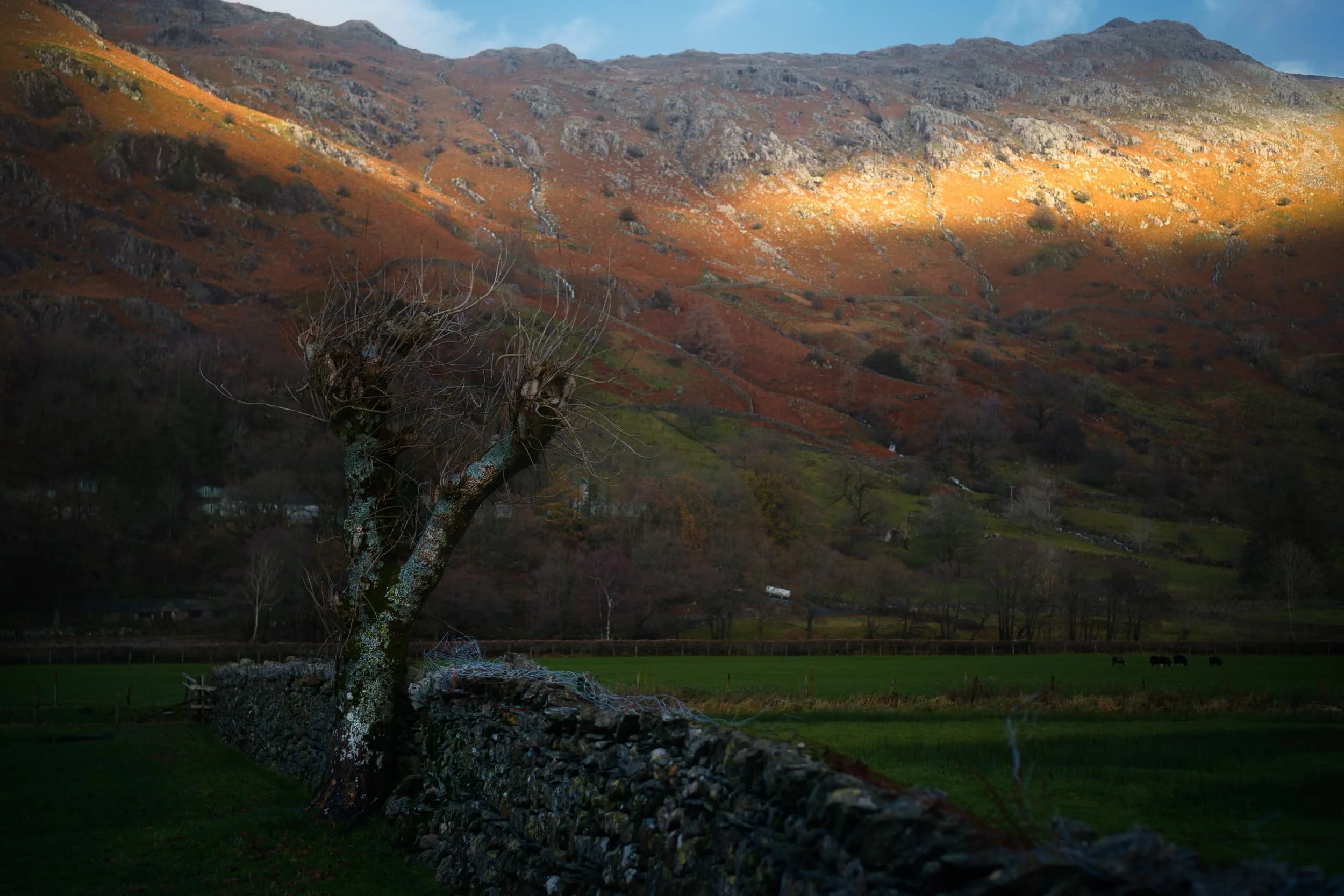 To the east of the Langdale Pikes is a wall of fells peaking at Broad Crag and Raw Pike, with a beam of light shooting across the face of the wall.