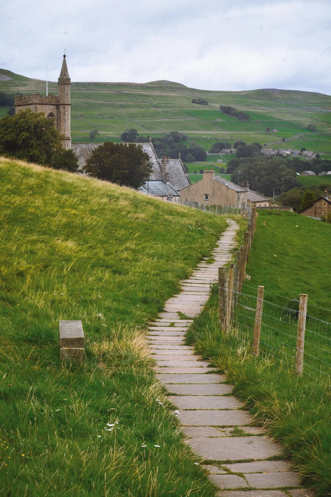  The well-maintained path takes you around the back of Hawes and opens up the views from above it. Here, the path serves as a leading line past St. Margaret&rsquo;s Church and over the buildings of Hawes, with the nub of Smuker Hill, part of Lovely Seat, visible. 