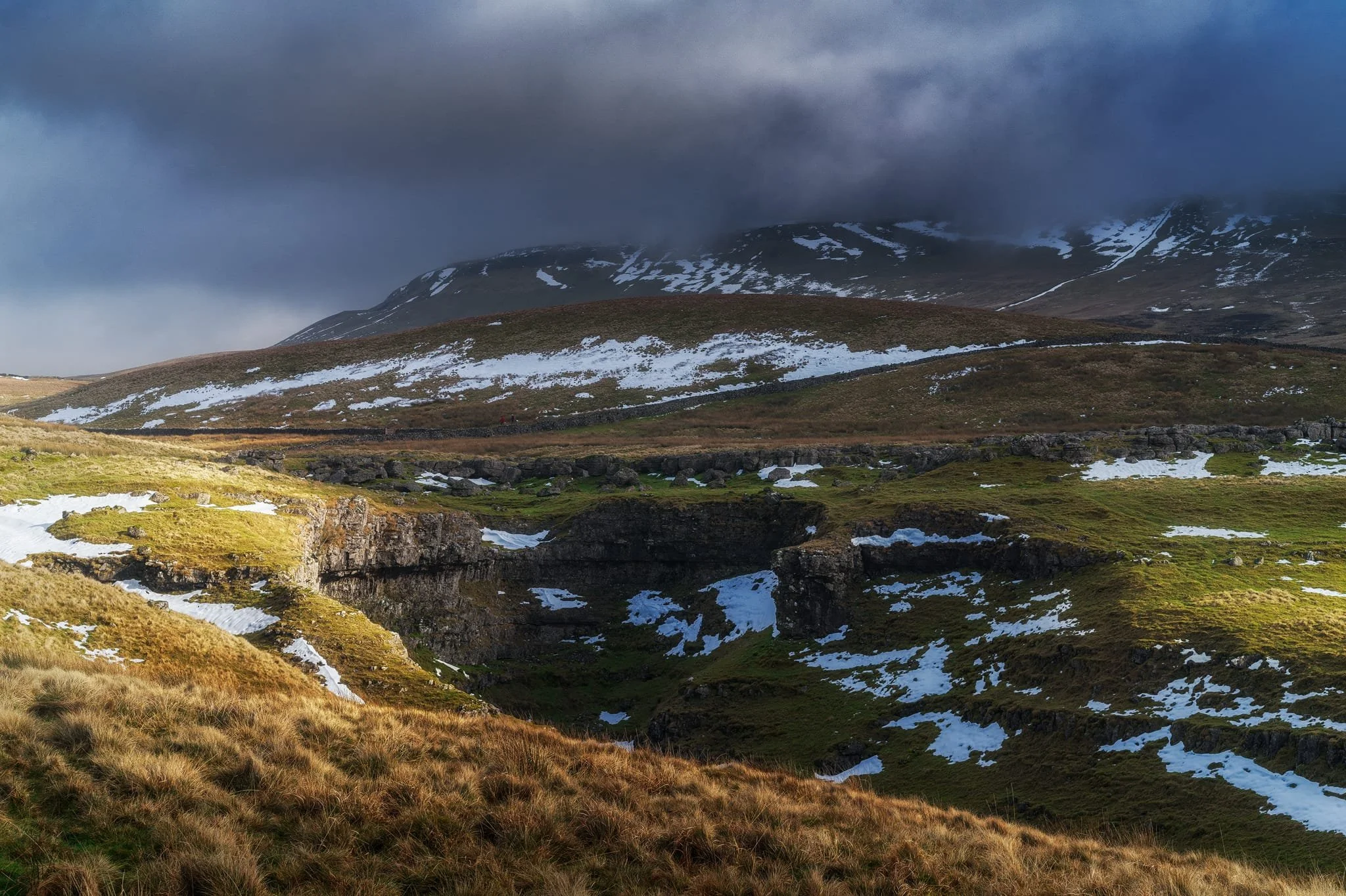 Further up the bridleway, the site of an extinct waterfall below Pen-y-Ghent, which is now obscured by clouds laden with snow. A burst of sun to our right picks out the details in the land.
