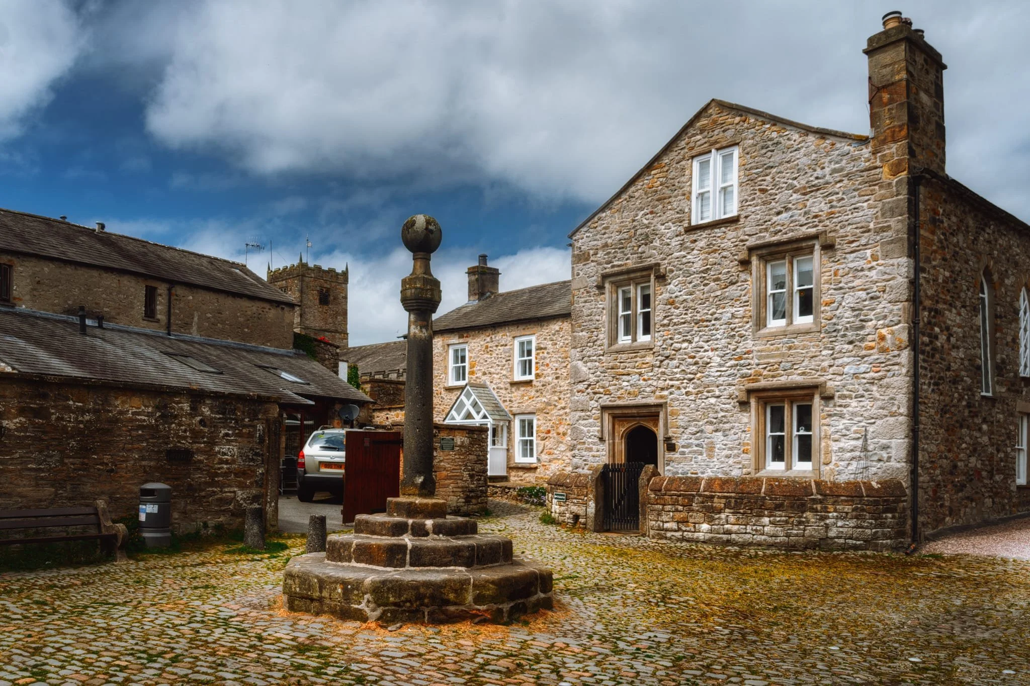  This little area down Red Dragon Yard and Mill Brow is known as Swine Market because, historically, that&rsquo;s what this area was. The pillar structure is the Old Market Cross, formerly located at the junction of Main Street, Market Street, and Mill Brow. It was relocated to Swine Market in 1822. The steps and crowning ball were a later addition.  