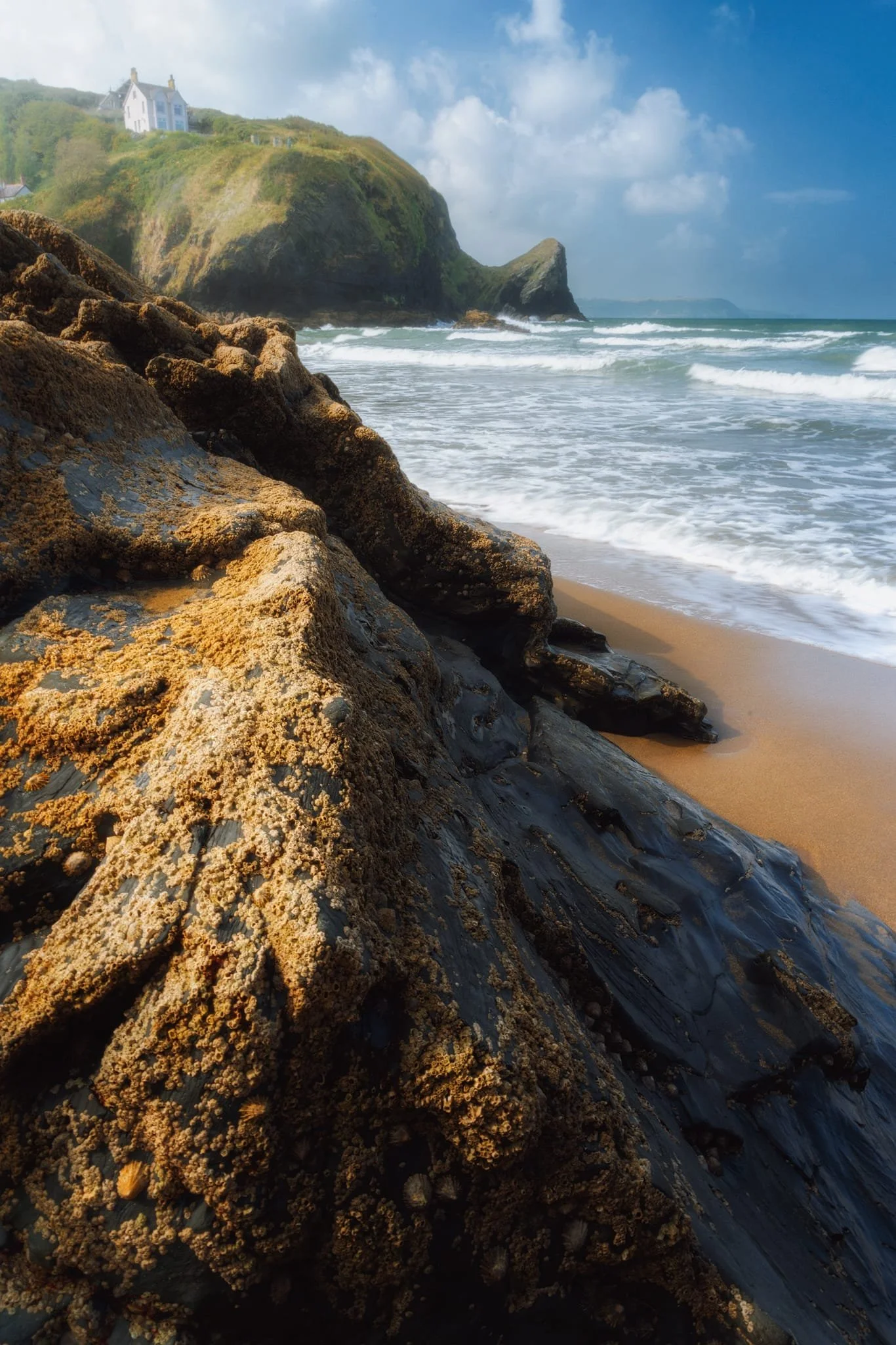  Looking to Llangrannog&rsquo;s southern cliffs, and the pointy crag of  Pen-rhip , I wait for the sun to strike this beach boulder and use the lighting as a leading line into the composition. 