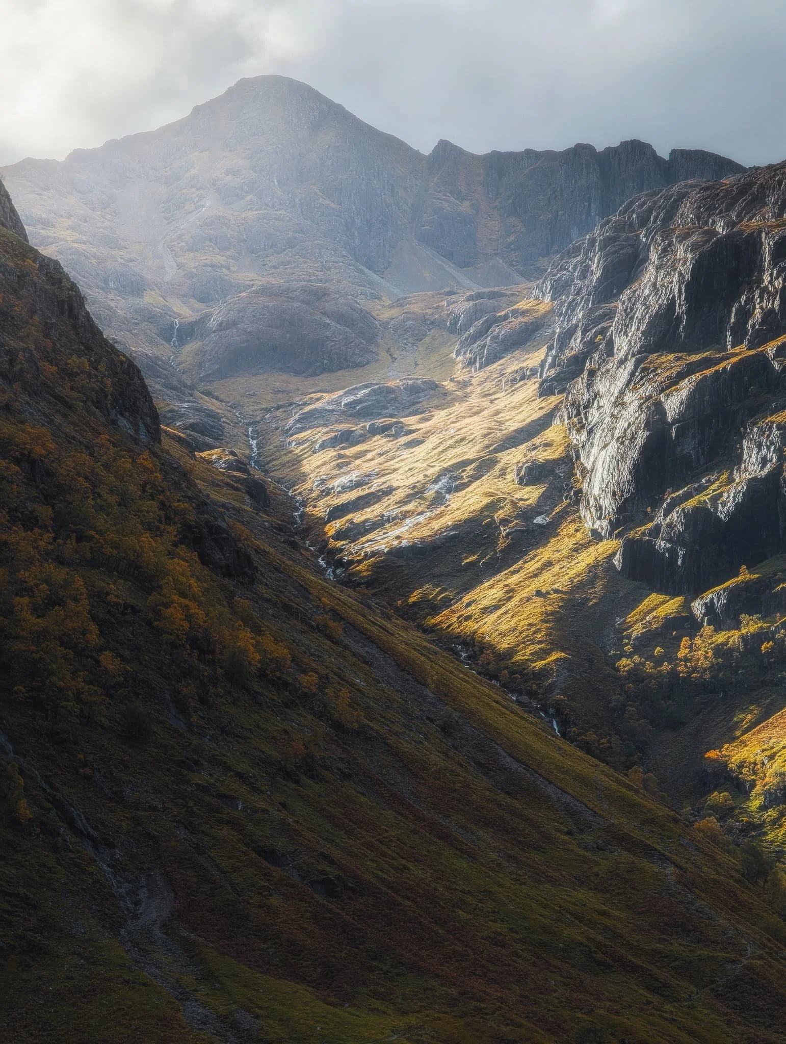 In the heart of Glencoe we stopped at the main car park and quickly located the trail east towards the head of the valley. Looming above us were the Three Sisters of Glencoe. With light piercing through the clouds above, I captured this 5x photo of Corrie nan Lochan’s crags getting drenched in light with Stob Corrie nan Lochan (1,115 m/3,658 ft) rising above.