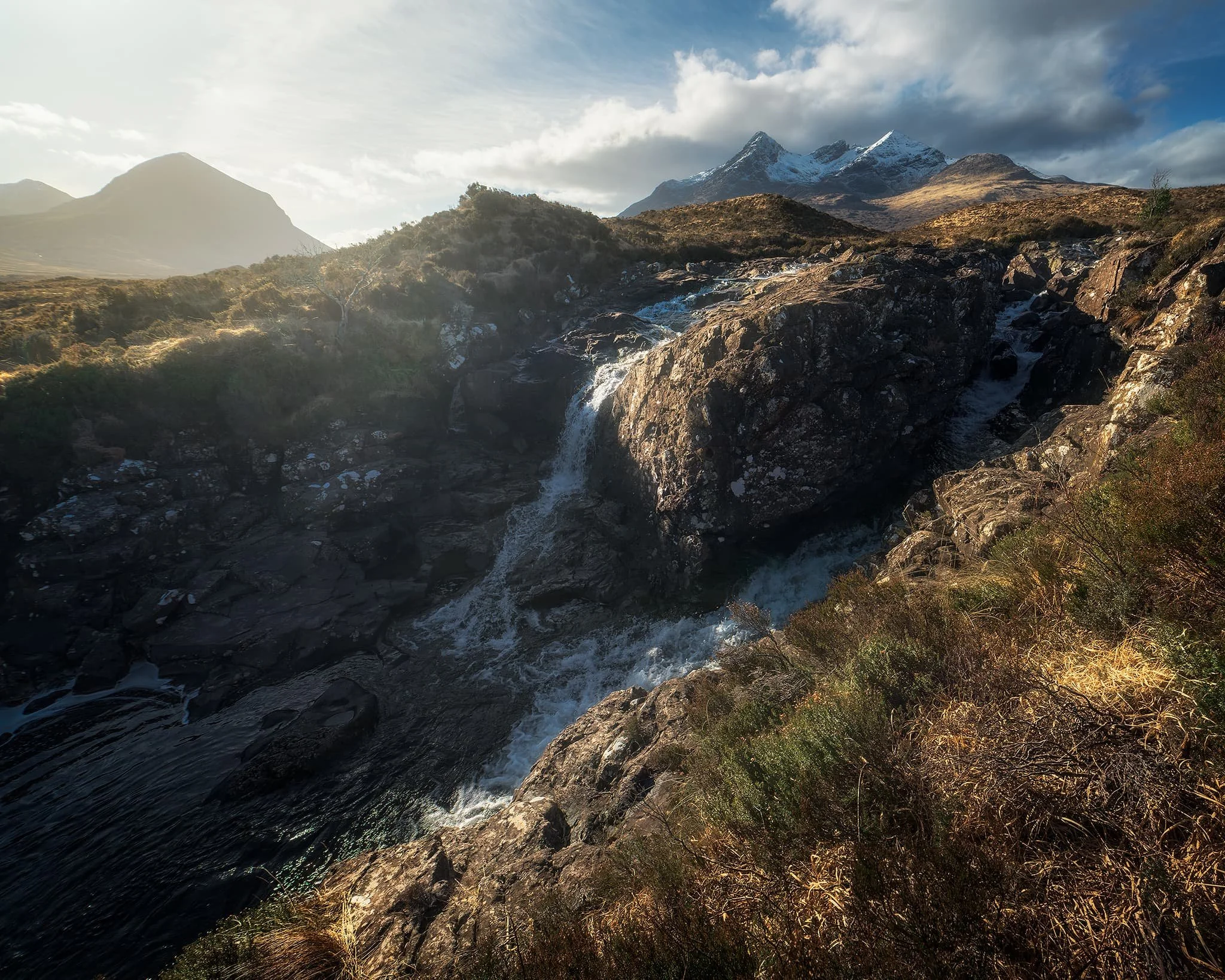  Afterwards, we began the hike up alongside one of Sligachan&rsquo;s many rivers, this one being the  Allt Dearg Mòr  (&ldquo;Great Red River&rdquo;). Numerous waterfalls can be found along the river, this one being one of the bigger ones. My ultra-wide 14mm lens was able to capture not only the entirety of the falls and the snow-capped Black Cuillins, but some of the Red Cuillins too. 