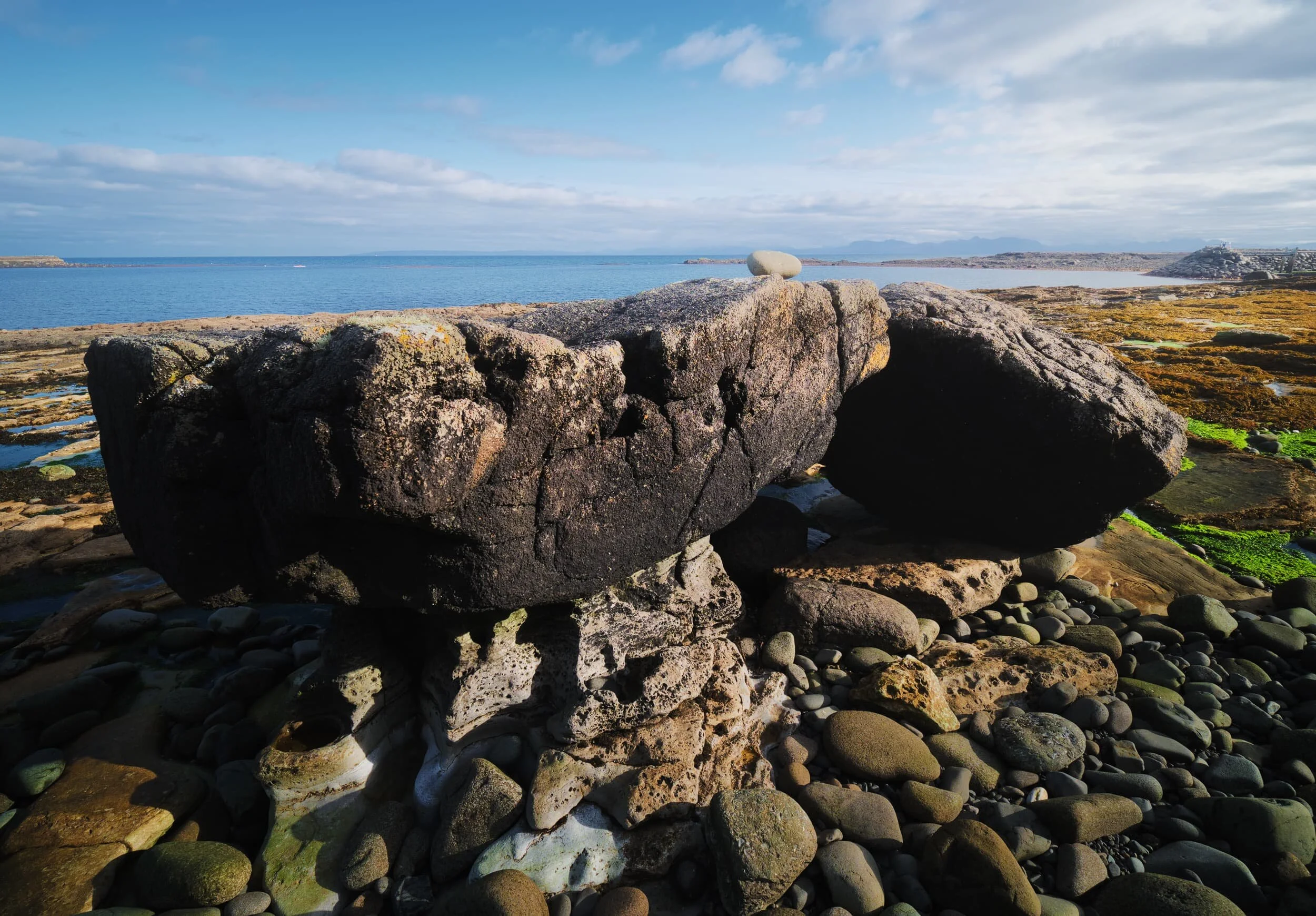 Two giant boulders lean on each other. In the distance are the mountains of Torridon and Applecross.