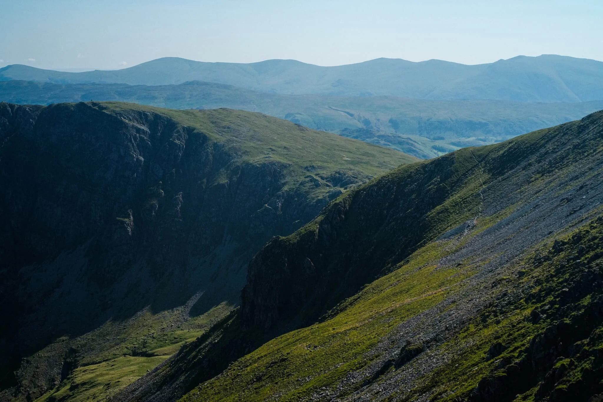 The view back east shows the sheer craggy drop of its northern face as well as the crags of High Spy. In the distance is the Helvellyn range.