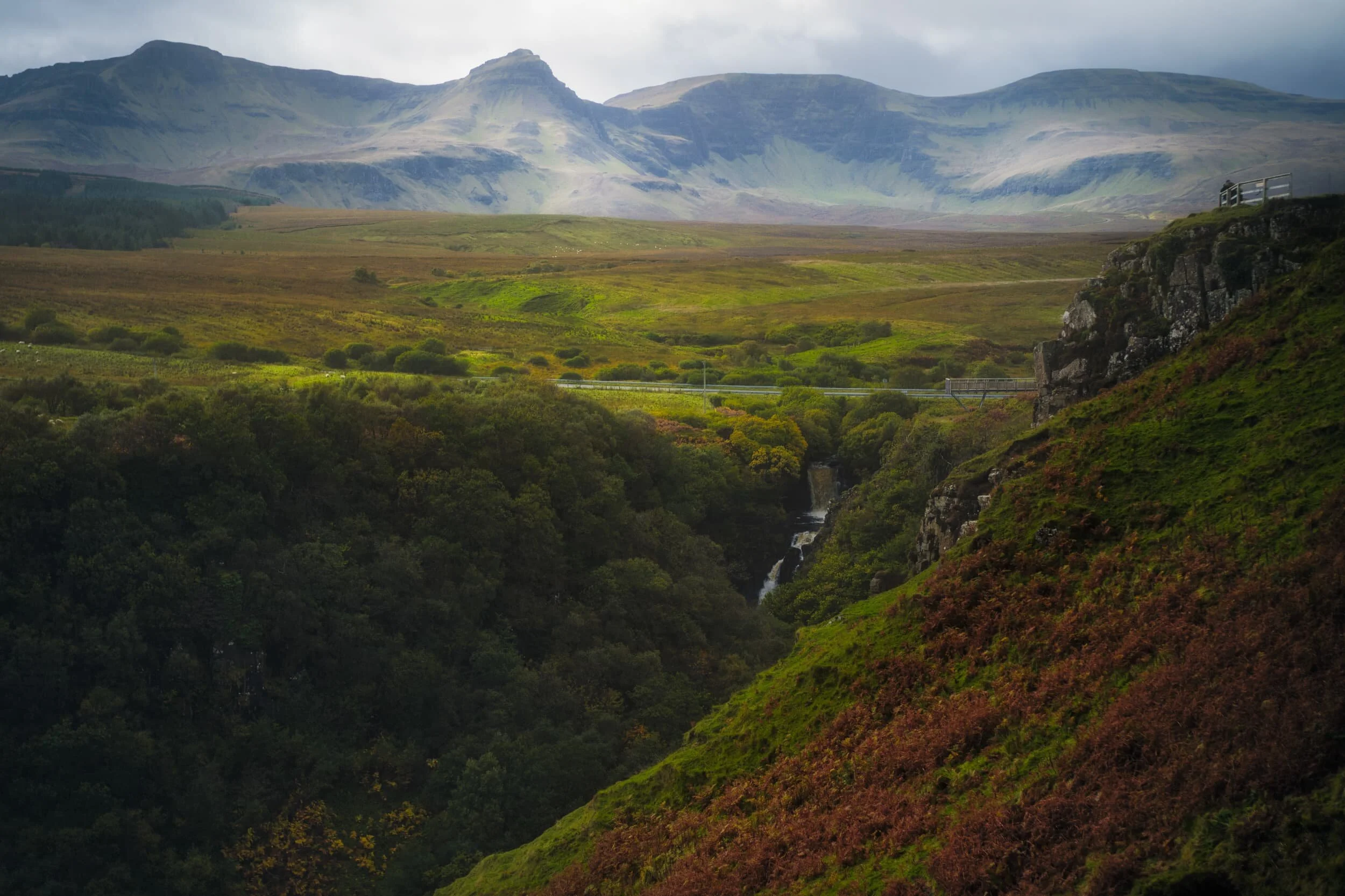  South of Kilt Rock and Mealt Falls there&rsquo;s another viewing platform, with ample parking, at Lealt Falls. The weather was extremely changeable that day, and I managed a 35mm shot of the upper waterfall with some brief sunlight on the land and the Trotternish landslip in the distance. The prominent peak featured is  Sgùrr a&rsquo; Mhadaidh Ruaidh  (pronounced SKOOR ah VAT-tee ROO-ah, meaning &ldquo;Peak of the red fox&rdquo;). 
