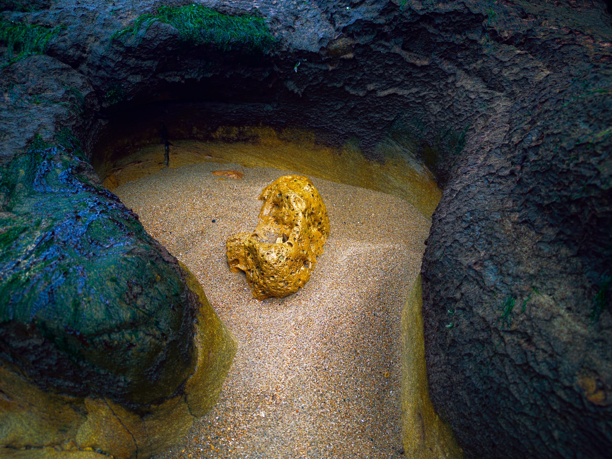 I gingerly navigated the rockfall of boulders, seeking more intimate compositions. Here, a golden rock in undisturbed sand is sheltered from the waves by the dark wave cut rocks around it.