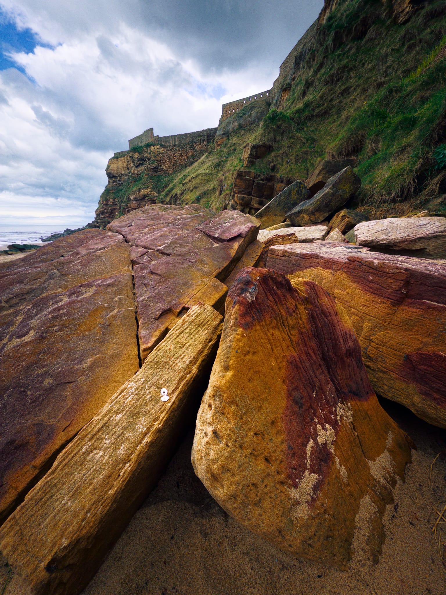 Fallen pieces of reddish sandstone, marked by ancient river patterns from around 300 million years ago, rest at the bottom of the same cliff that medieval builders of Tynemouth Priory instinctively chose as a stable and lasting foundation.